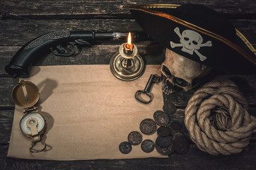 Pirate treasure map with copy space, pirate captain hat, compass, coins, human skull, mooring rope, musket and burning candle. Treasure hunter concept background.