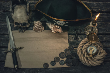 Pirate treasure map with copy space, pirate captain hat, compass, coins, human skull, mooring rope, dagger and burning candle. Treasure hunter concept background.