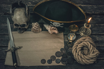 Pirate treasure map with copy space, pirate captain hat, compass, coins, human skull, mooring rope, dagger and burning candle. Treasure hunter concept background.