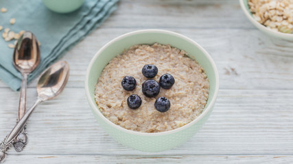 Oatmeal porridge bowl on the white wooden background.