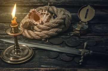 Pirate captain table with treasure coins, mooring rope, dagger, compass, seashell and burning table. Treasure hunter concept.