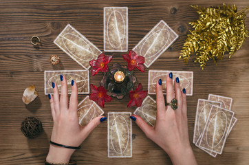 Tarot cards and hands of fortune teller on wooden table background.
