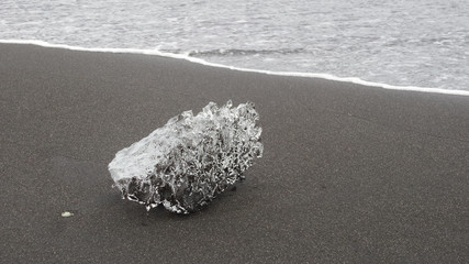 Eiskristall mit Lufteinschlüssen auf schwarzem Sandstrand in Island