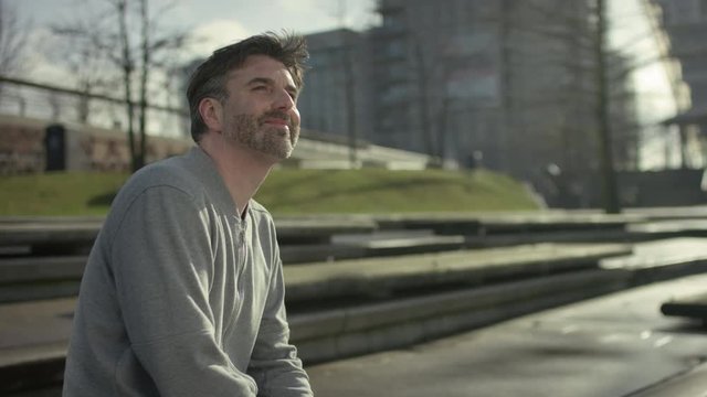 Smiling middle aged man is siiting on a bench in modern urban city in autumn