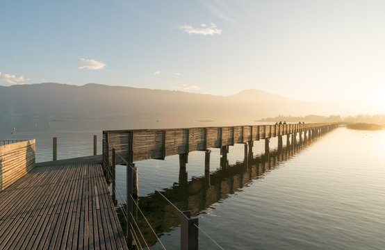 long wooden boardwalk pier over water in golden evening light with a mountain landscape silhouette in the background