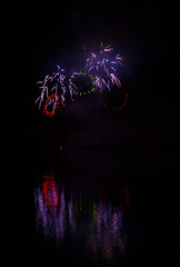 Red and green rings of rich fireworks over surface of Brno's Dam with reflection on the surface of lake