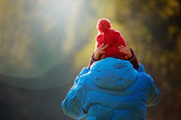woman in a blue down jacket is putting on a red cap. Woman is standing in the autumn forest on a...