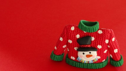 red sweater with green collar and sleeve cuffs white snowflakes and snowman with black hat and carrot nose isolated on a festive red background