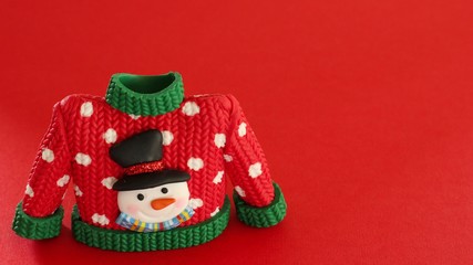 red sweater with green collar and sleeve cuffs white snowflakes and snowman with black hat and carrot nose isolated on festive red background with writing space