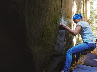 Fototapeta na wymiar A strong woman rock climber climbing a rock outdoors in forest. Athletes are bouldering outdoors.