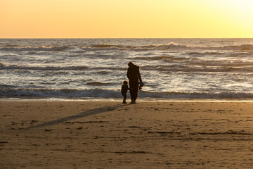 Woman with a child walking on beach in Katwijk at sunset. Netherlands