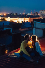 Loving couple is sitting on the roof of the house. Beautiful evening - obrazy, fototapety, plakaty