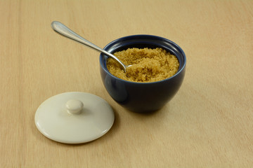 Brown sugar in blue sugar bowl with spoon inside and white lid on wooden table