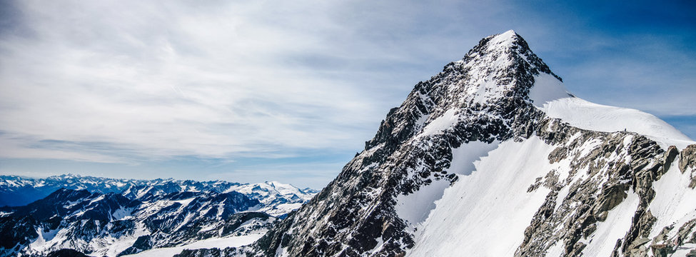 View of the highest austrian mountain Grossglockner. An alpine mountain landscape of High Taura with the summit of Grossgloner. Alpinist ascent route to the summit. Snow, rocks and sharp ridge.