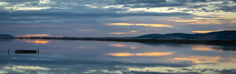 Fototapeta na wymiar panorama sur un étang au coucher de soleil avec une barque et des flamants roses au fond