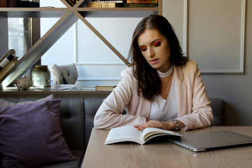 Young beautiful woman with a beautiful face, reading a book, sitting in a modern cafe interior.