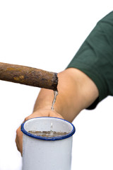 Water flows from a rusty pipe into a cup held by one hand