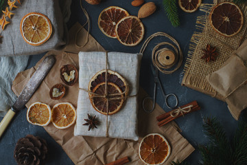 Christmas or New Year composition with handmade gifts, dry oranges, cinnamon, fir tree on dark stone table. Holidays preparations, hugge concept, top view, selective focus