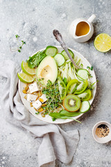 Vegan, detox Buddha bowl with quinoa, avocado, zucchini noodles, cucumber, tomato, lime, kiwi, tofu, spinach, micro greens, pepitas. Grey concrete background