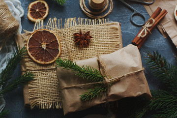 Christmas or New Year composition with handmade gifts, dry oranges, cinnamon, fir tree on dark stone table. Holidays preparations, hugge concept, top view, selective focus
