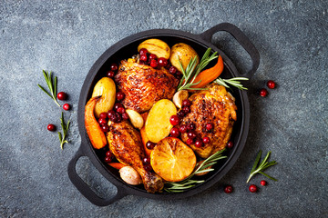 Roasted chicken legs with root vegetables, lemon, garlic, cranberry and rosemary on pan, on black...