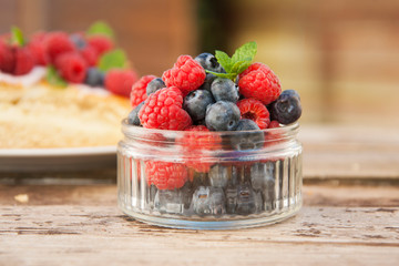 Small glass bowl full of blueberries and raspberries, ready to eat, placed on rustic wood desk.