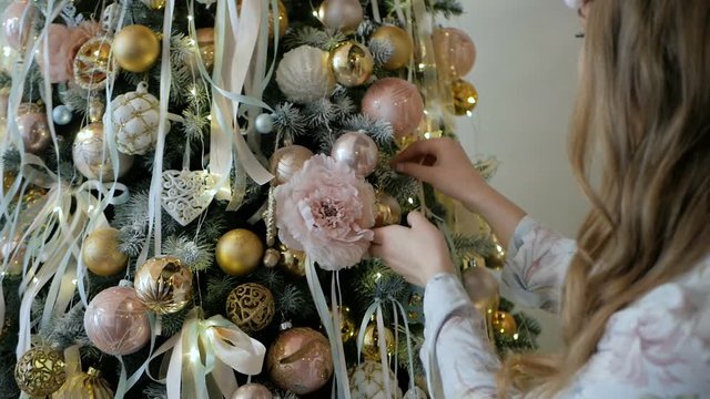 Beautiful blonde girl in pajamas decorating the Christmas tree