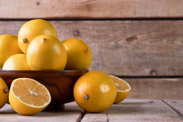Fresh lemons in a wooden bowl on wood background with copy space