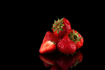 Macro image of fresh red strawberries group isolated at black background with reflection.
