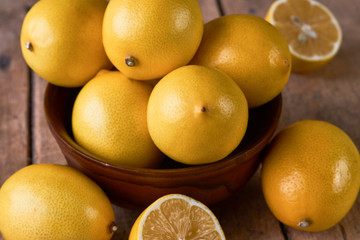 Yellow lemons in a wooden bowl on wood background.