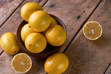 Yellow lemons in a wooden bowl on wood background.