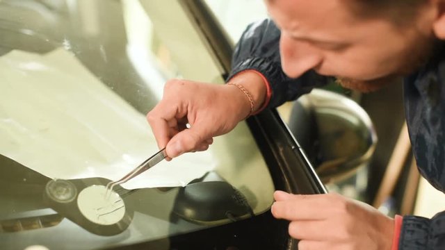 Close-up of a man professionally in the workshop engaged in eliminating cracks on the windshield of the car. Filling the crack with polymer