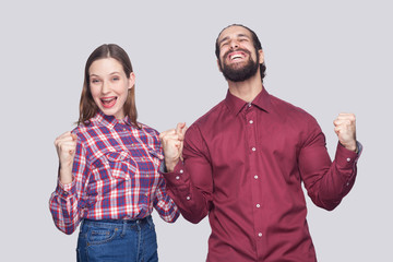 Portrait of happy amazed bearded man with black collected hair and woman in casual style standing with fist and celebrating their victory. indoor studio shot, isolated on gray background.