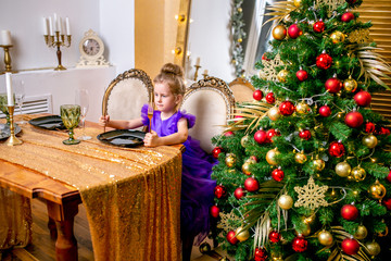 Pretty little girl 4 years old in a blue dress. The child at the table before the Christmas dinner