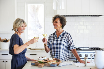 Senior women friends drinking wine in kitchen