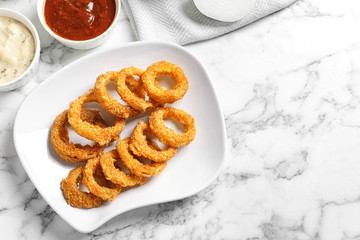 Homemade crunchy fried onion rings with sauces on marble table, top view. Space for text