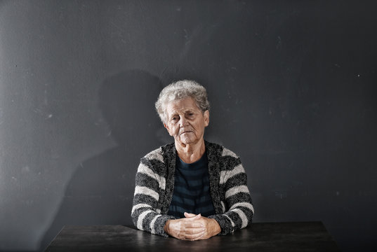 Portrait of poor elderly woman sitting at table on dark background