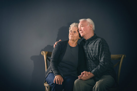 Poor pensive elderly couple on dark background