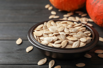 Full bowl of raw pumpkin seeds on wooden table