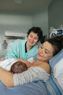 Smiling birth doctor helping new mother with breast feeding in hospital