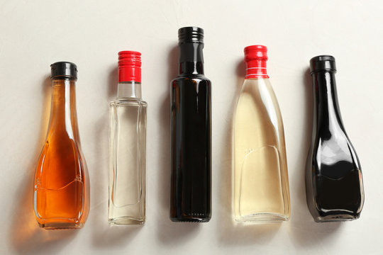 Bottles with different kinds of vinegar on light table, top view
