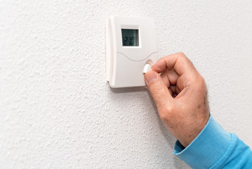 Man hand adjusting thermostat at home. Celsius temperature scale.