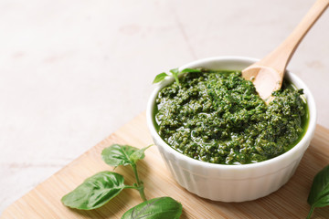 Board with homemade basil pesto sauce in bowl on table