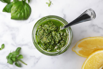 Homemade basil pesto sauce in glass jar on table, top view