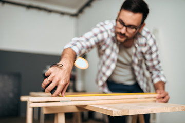 Young man working on a DIY project measuring wood. Focus on the foreground.
