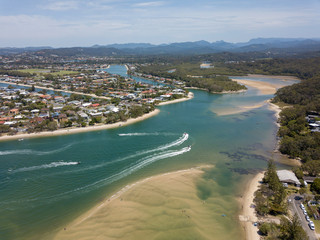 A boat driving down the waterways in the Gold coast, you can see housing, sandbars and part of the national park