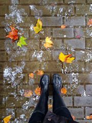 Top view of city pavement in a winter or autumn rainy day. Feet in rubber boots with rain drops and...