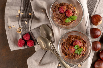 Glass cups of chocolate and chestnuts mousse with roasted almonds and oats decorated with raspberry and mint leaves