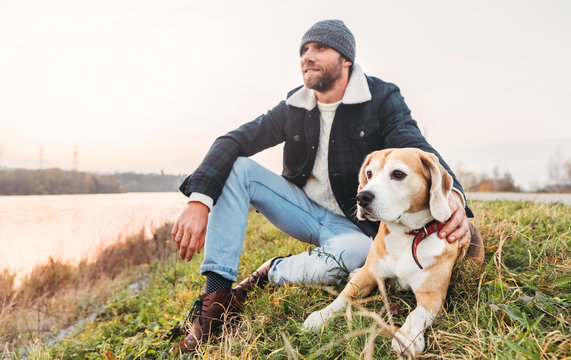Man with beagle dog sitting together near the lake