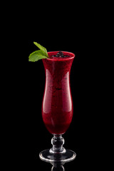 Glass of red cherry fresh shake decorated with black currant and mint isolated at black background.